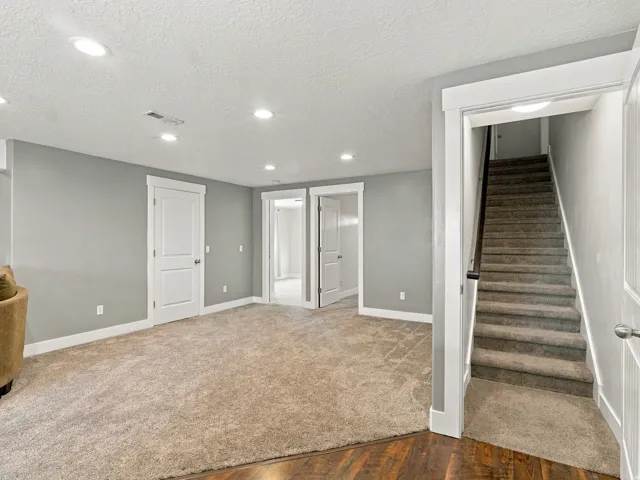 Recessed lighting, wood-finish flooring, light gray wall paint, and gray carpeted stairs