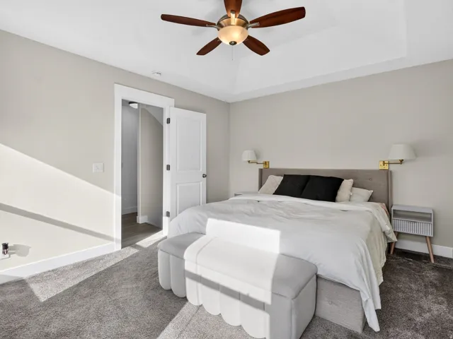 Tray ceiling with a ceiling fan, wall-mounted sconces, and carpeting