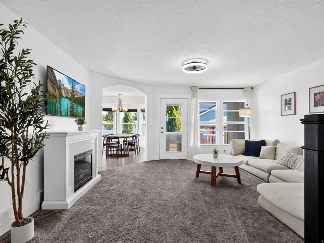 Bright living area featuring carpet flooring, a white mantel with an electric fireplace, an arched entryway, and multiple windows providing natural light