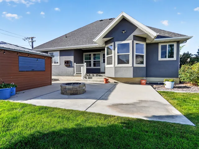 Rear exterior featuring a concrete patio, built-in stone fire pit, and an auxiliary structure