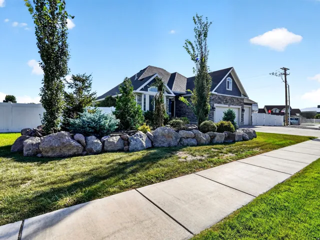 Stone and siding exterior with a gabled roofline, featuring a two-car garage, mature landscaping, and a rock retaining wall