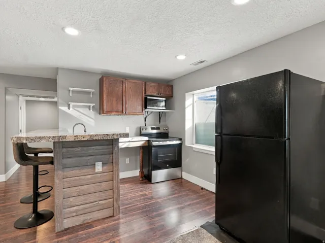 Kitchen featuring a peninsula with a stone-finish countertop, wood-finish flooring, recessed lighting, wood cabinetry, and stainless steel appliances