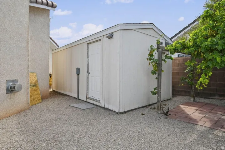 Detached storage shed with a panel door, gravel ground cover, and a brick paver patio