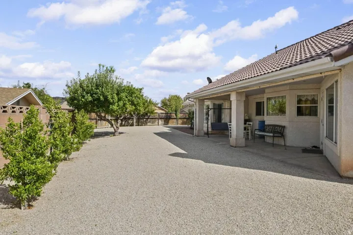 Spacious outdoor area featuring a covered patio with supporting columns, a tile roof, mature trees, and a gravel-covered surface