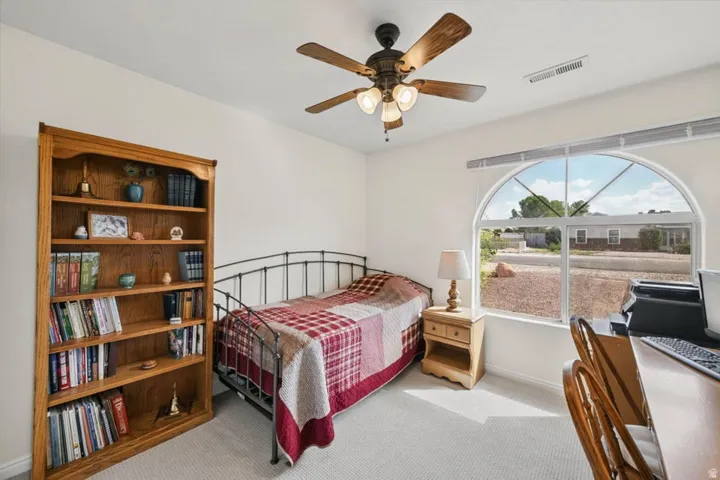 Arched window with exterior views, ceiling fan light fixture, and light-colored carpeting