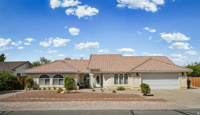 Stucco exterior with a tile roof, arched windows, an attached garage, a covered entry, and a gravel and rock front yard