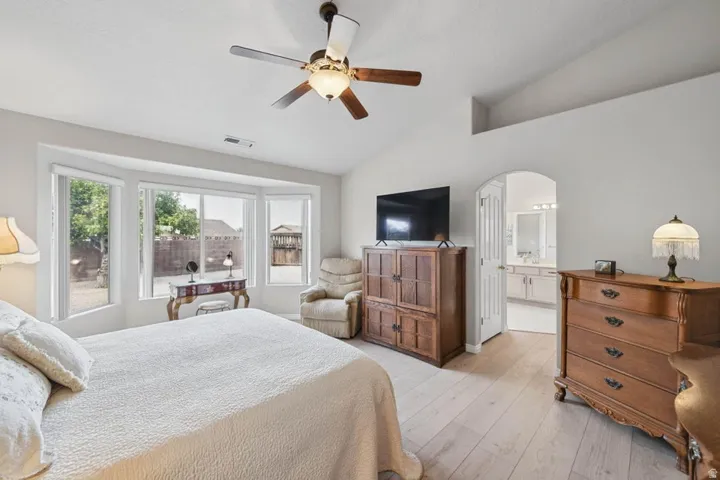 Vaulted ceiling with a ceiling fan, bay windows, wood-finish flooring, and an arched doorway leading to an adjoining space