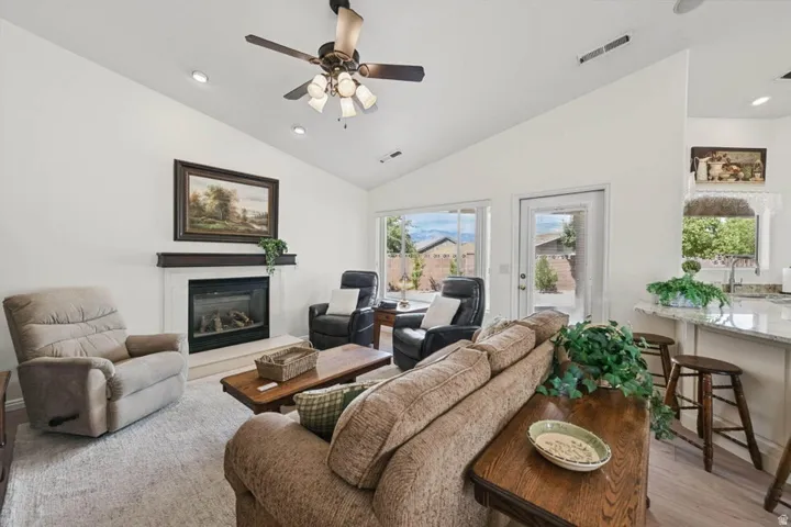 Vaulted ceiling, ceiling fan, built-in fireplace with white mantel, glass-paneled exterior door, and recessed lighting
