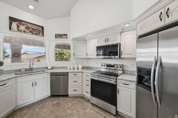 White cabinetry, stainless steel appliances, granite countertops, tile flooring, and recessed lighting