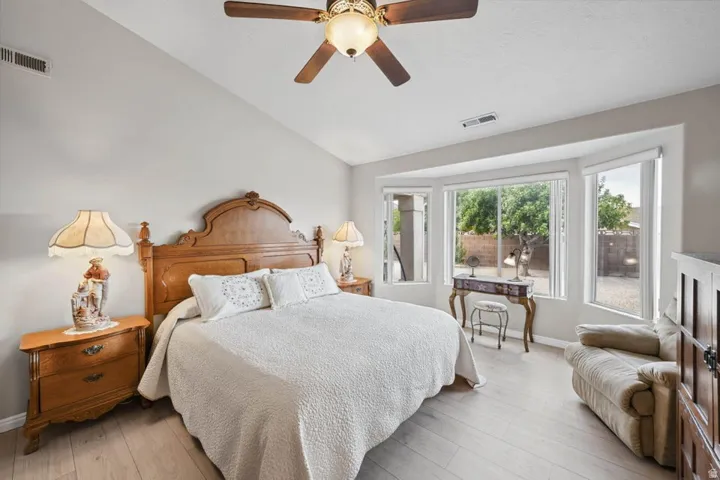 Vaulted ceiling, ceiling fan, expansive bay window, wood-finish flooring, and neutral wall tones
