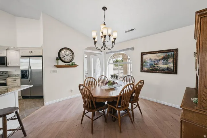 Vaulted ceiling, wood-finish flooring, arched doorway, recessed lighting, and a chandelier with glass shades
