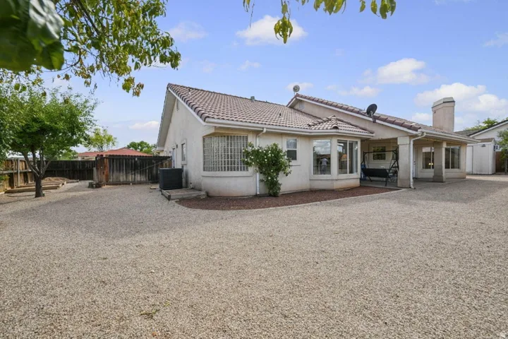 Spacious gravel yard with perimeter fencing, covered patio, stucco exterior, and a prominent chimney