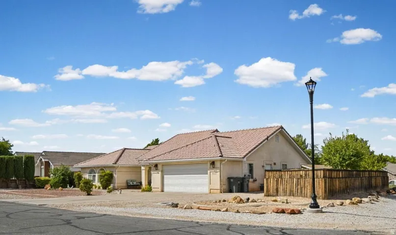 Stucco exterior with a tile roof, an attached garage, a paved driveway, and a wood privacy fence