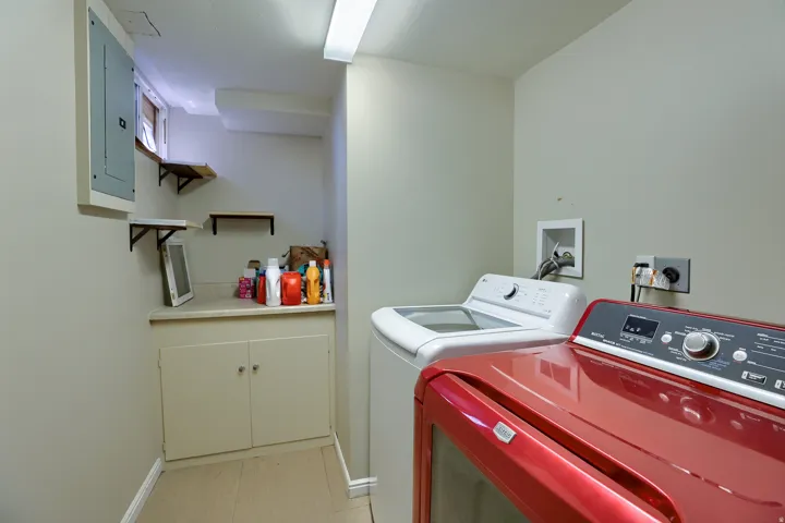 Functional laundry area featuring light-toned walls, built-in lower cabinetry, a countertop, and wall-mounted shelving