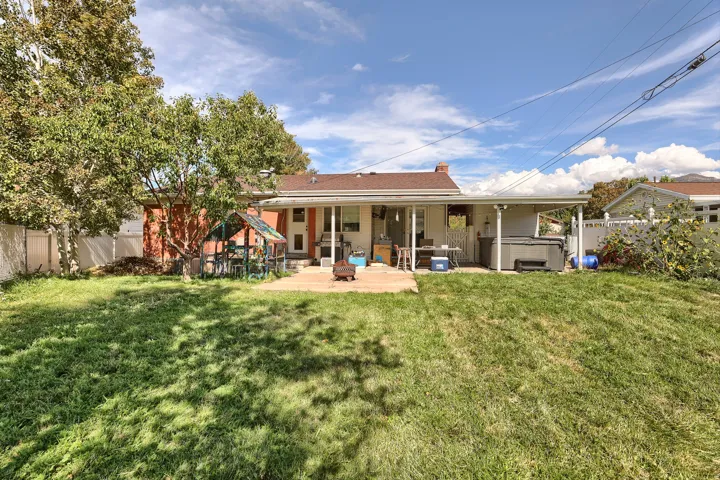Expansive grass lawn with mature trees, a paved patio area, and a covered patio extension
