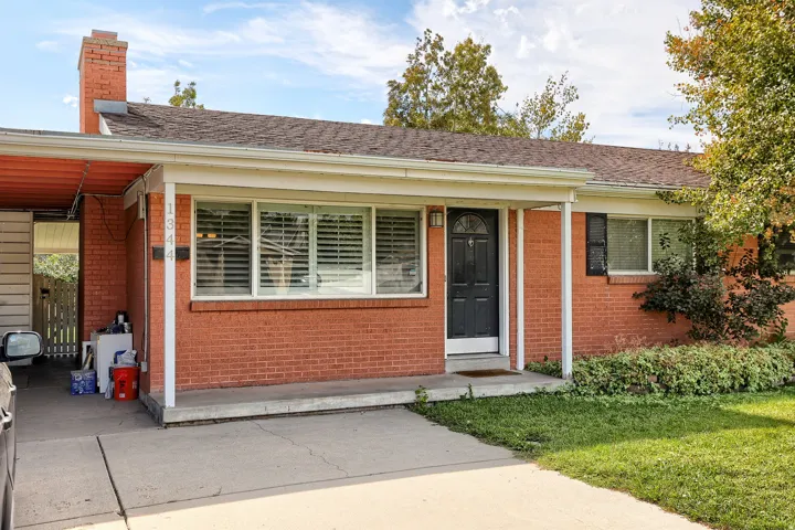 Brick facade with a dark entry door, multiple front windows, a covered front porch, and a side carport