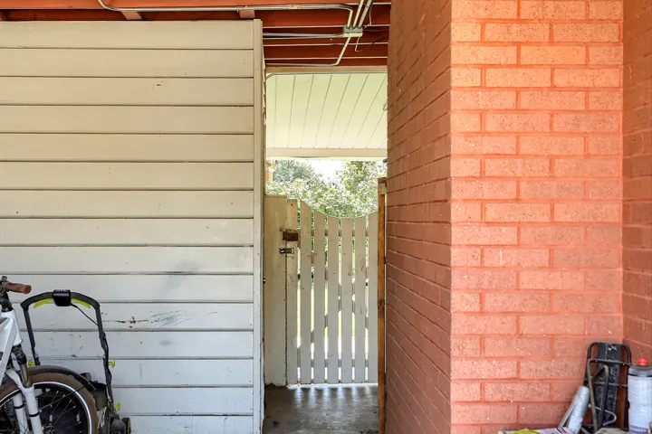 Red brick wall, white horizontal paneling, concrete flooring, and a white picket gate