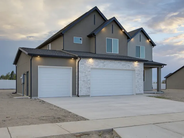 Stucco exterior with stone veneer accents, multi-car garage, concrete driveway, and covered entry