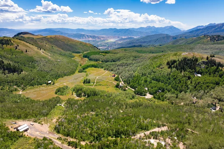 Expansive mountainous landscape with numerous trees, open fields, and distant structures