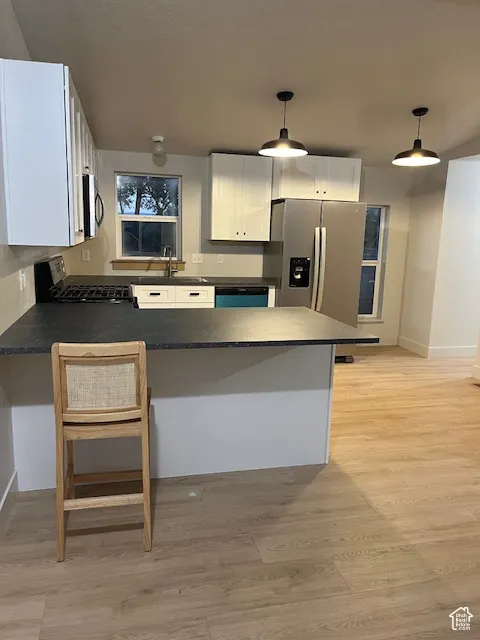 Kitchen featuring white cabinetry, dark countertops, stainless steel appliances, and wood-finish flooring