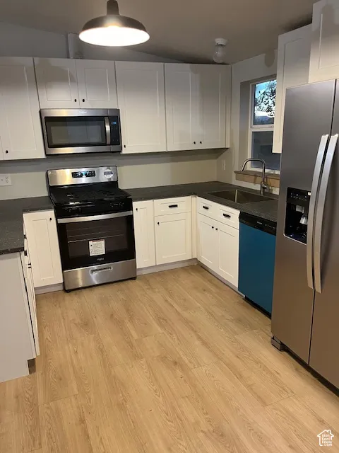 Kitchen featuring wood-finish flooring, white cabinetry, dark countertops, a stainless steel range, and a stainless steel microwave