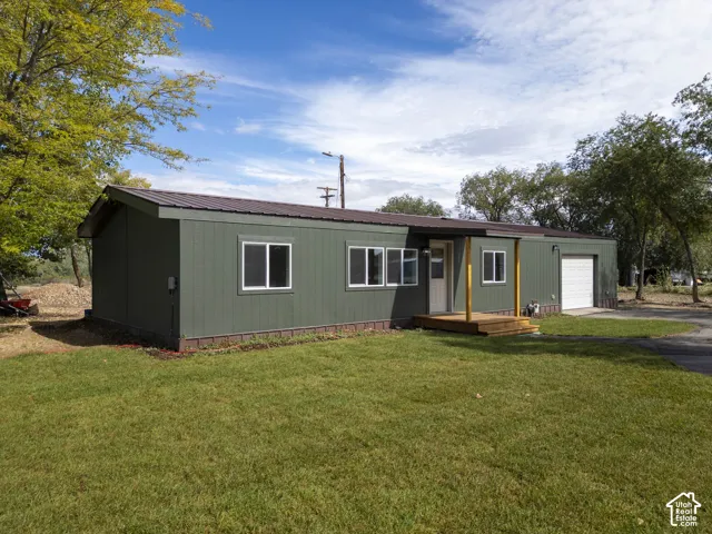 Green siding exterior with white window trim, a brown metal roof, a wooden front porch, and an attached garage with a roll-up door
