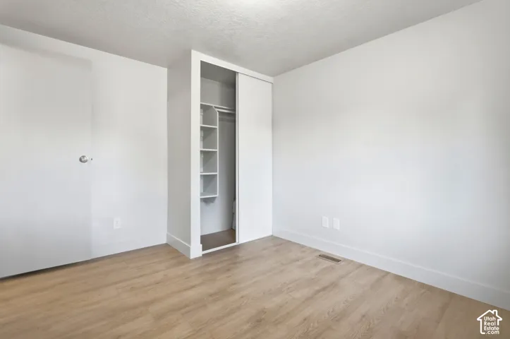 Wood-finish flooring with white baseboards, a built-in closet with sliding doors, and integrated shelving