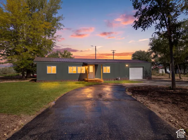 Paved driveway leading to a residence with a metal roof, attached garage, and front porch