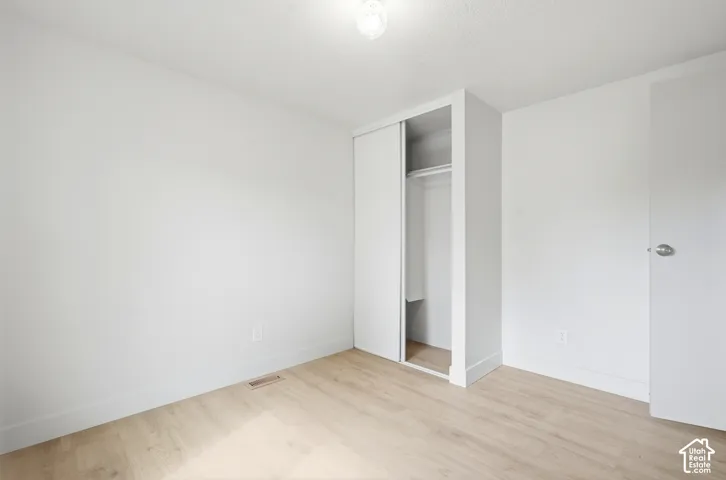 Light-toned wood-finish flooring, white painted walls, built-in closet with sliding doors, and a ceiling-mounted light fixture