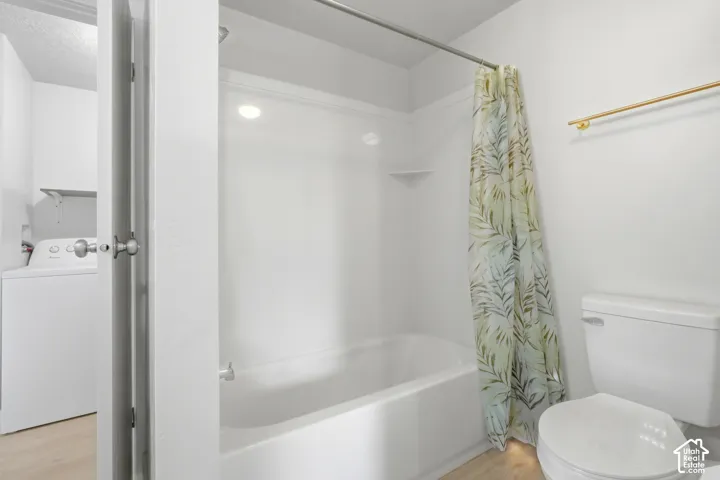 White bathtub with an integrated shower, adjacent white toilet, and wood-finish flooring
