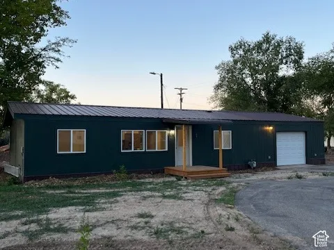 Dark green metal siding, brown metal roof, light wood porch, attached garage with white door, paved driveway