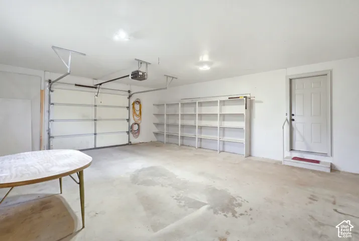 Attached two-car garage with concrete flooring, built-in shelving, and white paneled door