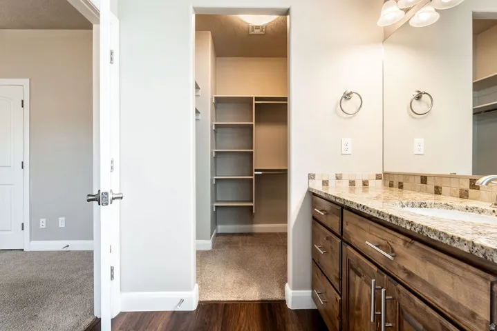 Vanity with wood-finish cabinetry, granite-style countertop, and a tiled backsplash