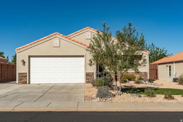 Stucco exterior with stone-look accents, concrete tile roof, attached garage, and a drought-tolerant front yard with a mature tree