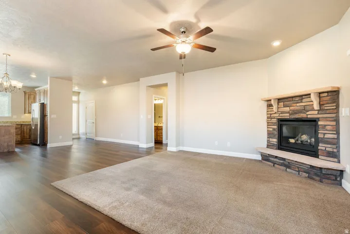 Living space featuring a stone-clad fireplace with a hearth, wood-finish flooring, recessed lighting, and a ceiling fan