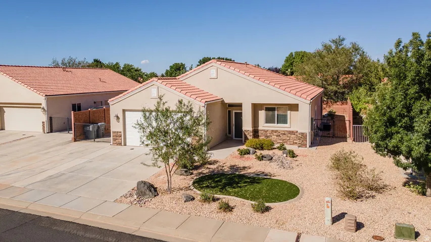 Stucco exterior with stone accents, concrete tile roofing, attached garage, and a low-maintenance xeriscaped front yard