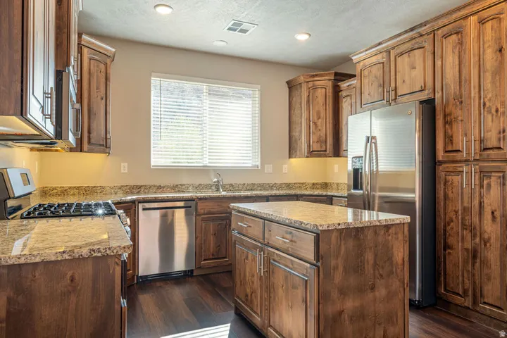 Kitchen featuring rich wood cabinetry, stainless steel appliances, speckled countertops, a central island, and recessed lighting