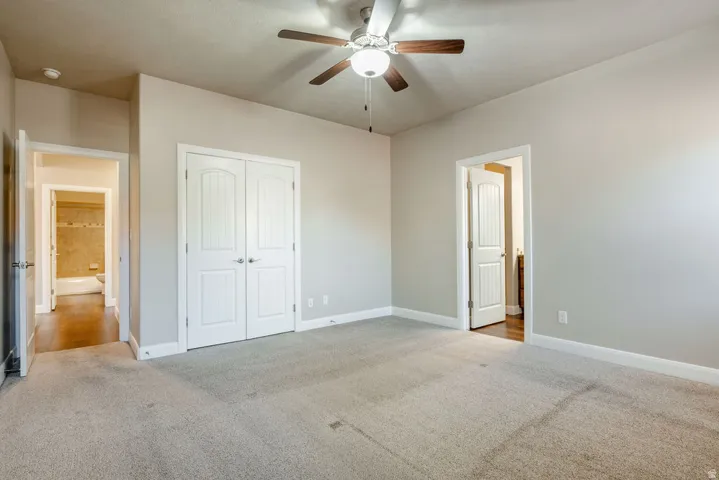 Plush carpeted flooring, a ceiling fan with light fixture, and white interior doors