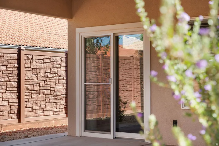 Sliding glass door access, stucco exterior, concrete patio, and stone veneer privacy wall