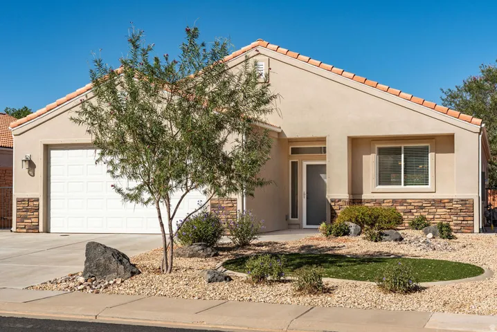 Stucco exterior with stone accent detailing, a tile roof, a two-car garage, and desert-style landscaping