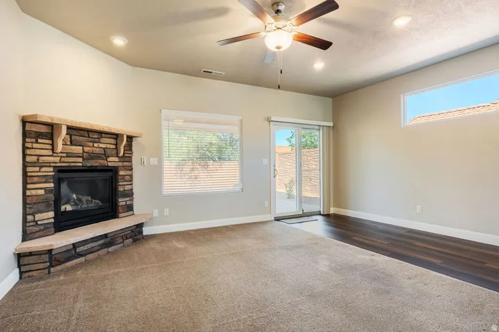 Stone-clad fireplace, ceiling fan with integrated lighting, recessed lighting, sliding glass door, and wood-finish flooring