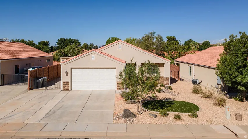 Stucco exterior with stone accents, attached garage, tile roof, and desert-style landscaping