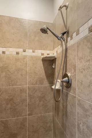 Tiled shower featuring a decorative mosaic accent band, brushed nickel fixtures, and a built-in corner shelf