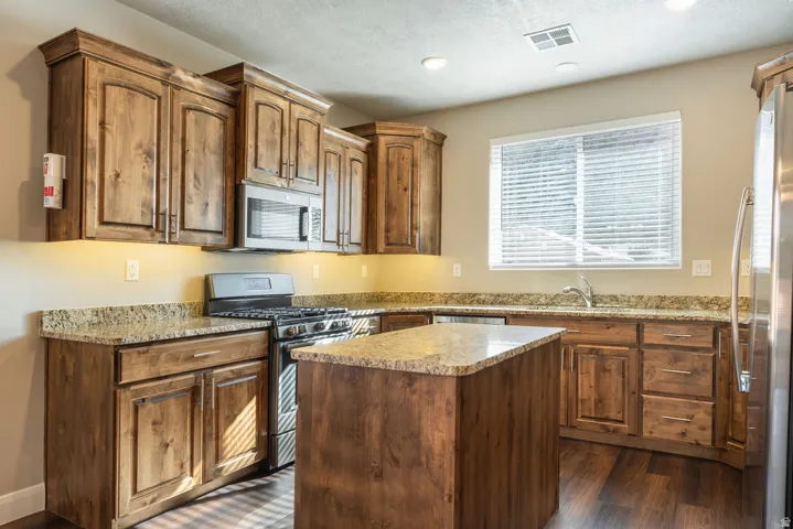 Kitchen featuring wood-finish cabinetry, under-cabinet lighting, a central island, and stone countertops