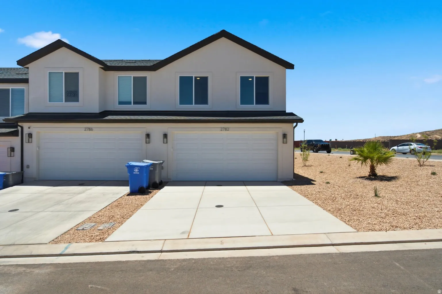 Two-story stucco exterior with dark trim, dual garage doors, and individual driveways
