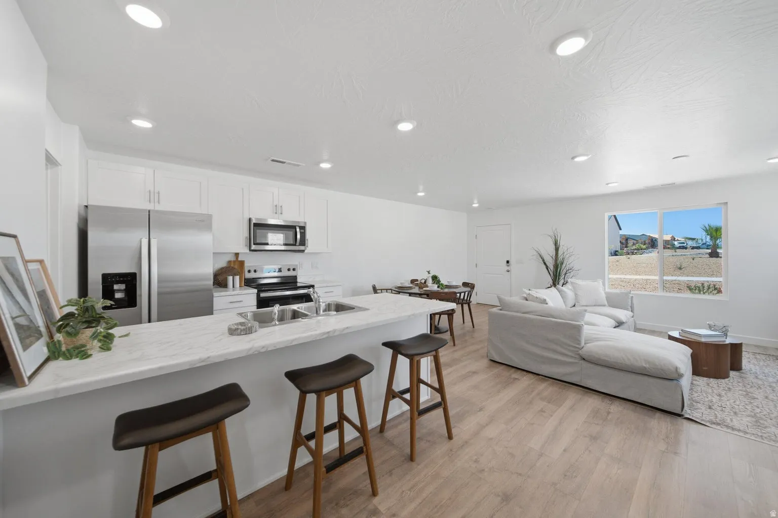 Kitchen island with a light-toned countertop, stainless steel appliances, white cabinetry, recessed lighting, and wood-finish flooring