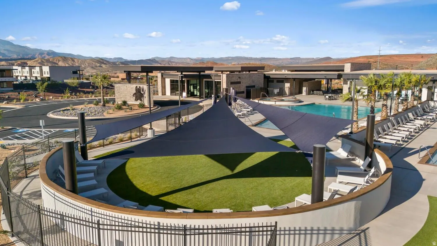 Outdoor amphitheater with artificial turf, multiple shade sails, and surrounding pool deck
