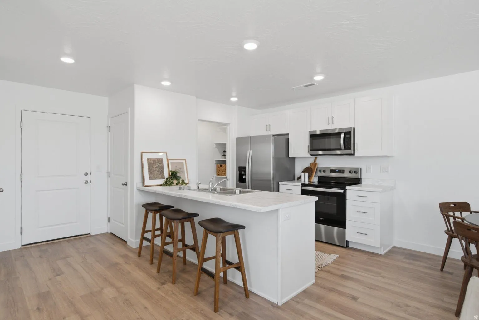 Kitchen featuring white cabinetry, stainless steel appliances, a center island with countertop seating, recessed lighting, and wood-finish flooring