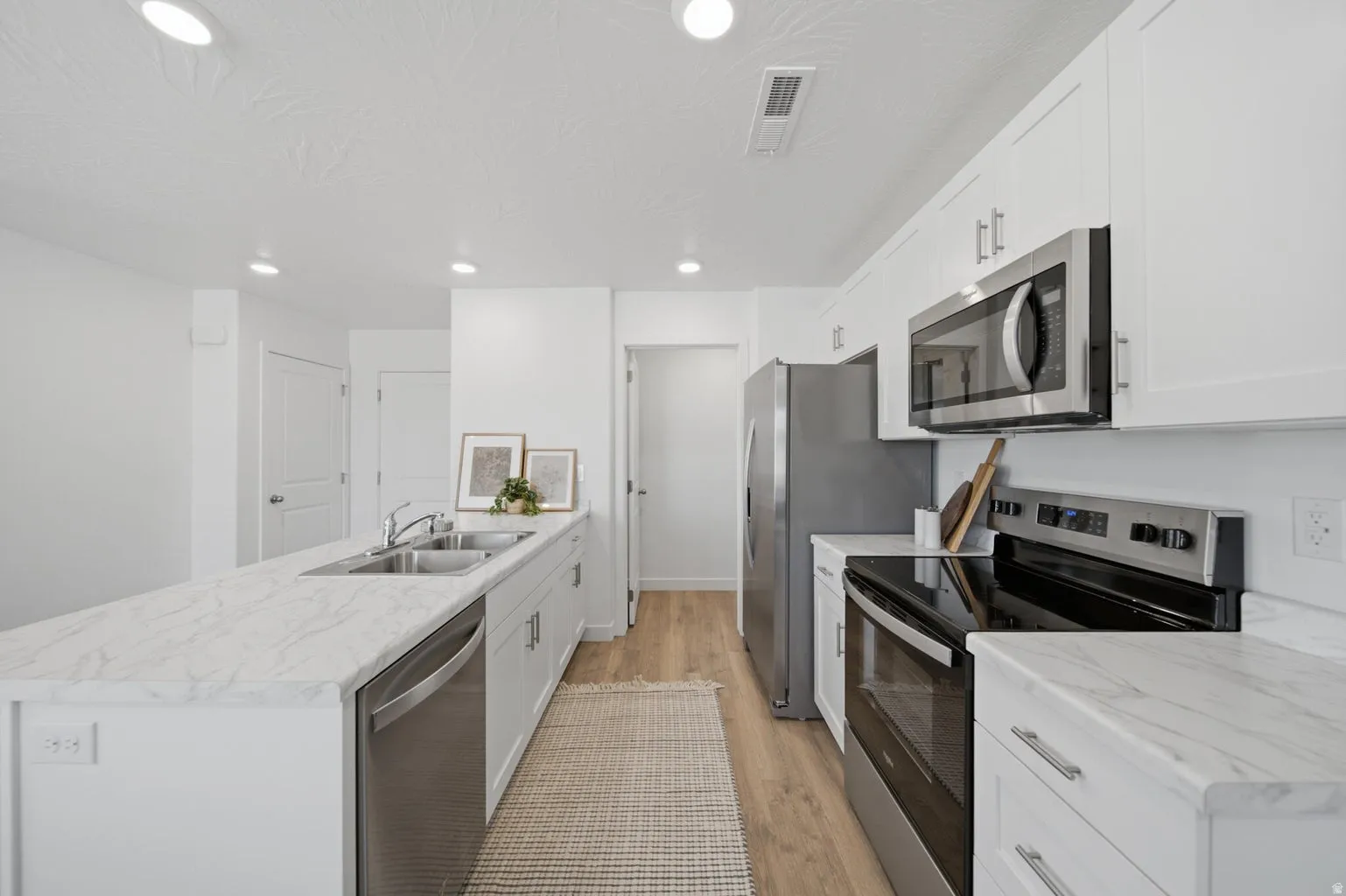 Kitchen featuring white cabinetry, stainless steel appliances, wood-finish flooring, recessed lighting, and light-toned countertops