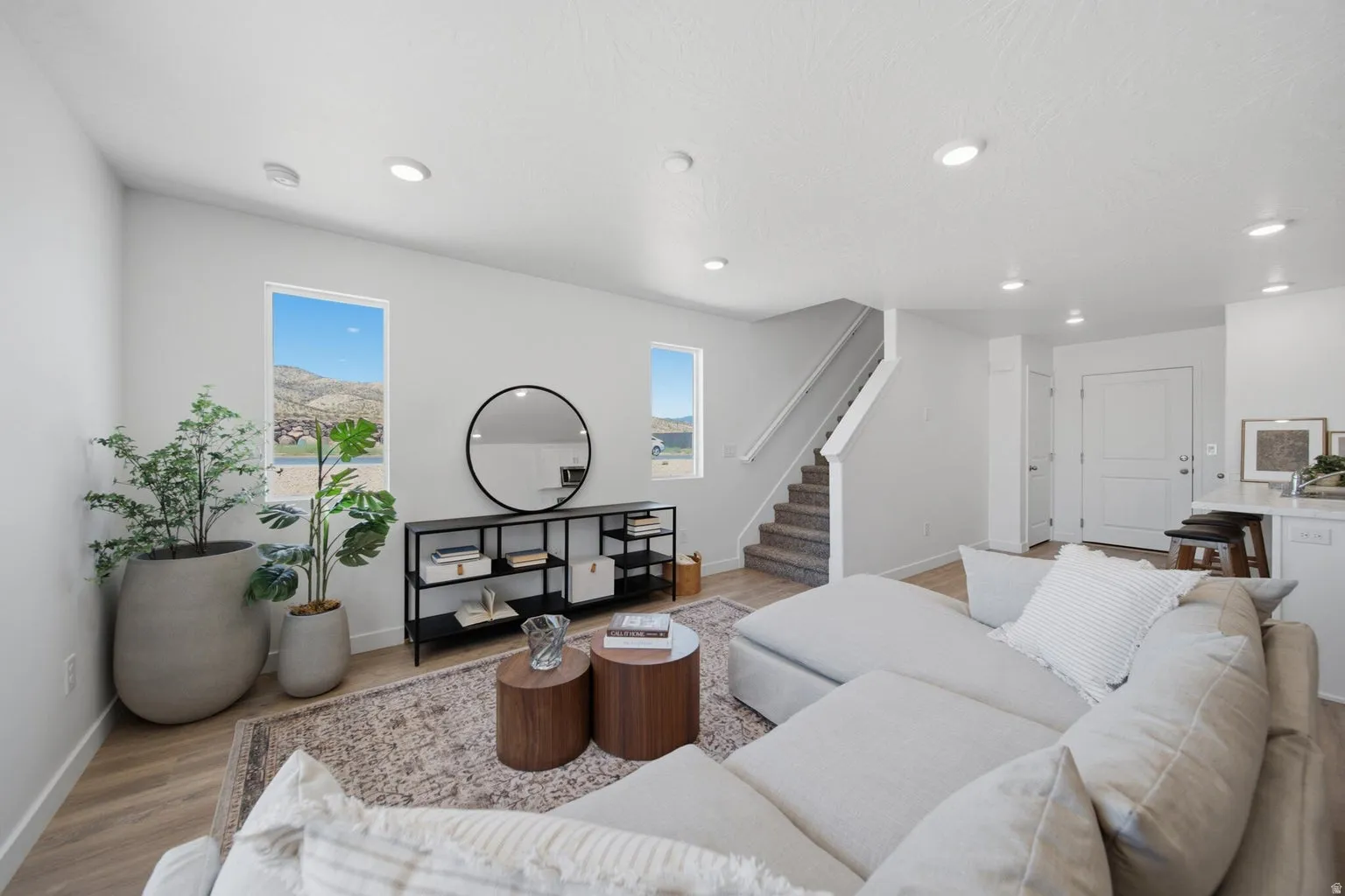 Recessed lighting, wood-finish flooring, staircase with carpeted treads, white interior doors, and a partial kitchen counter with bar seating